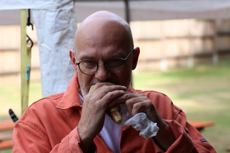 Mann mit Brille und orangefarbener Jacke beißt in ein Brötchen