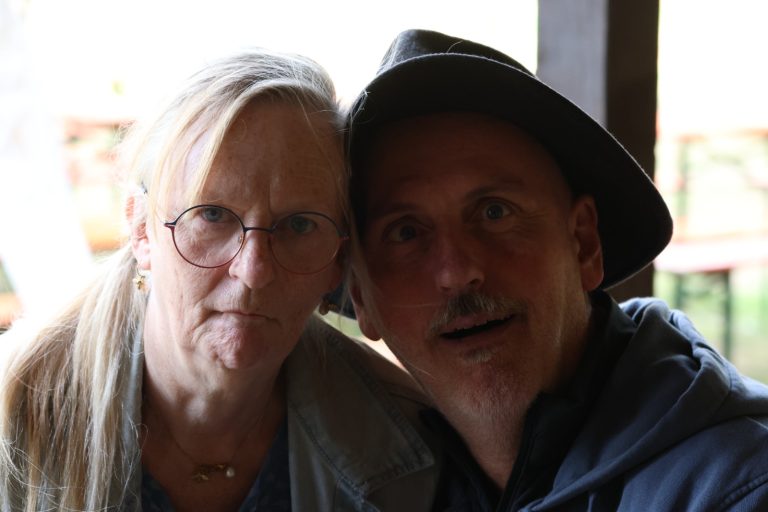 Frau mit Brille und Mann mit schwarzem Hut rücken für ein gemeinsames Foto zusammen