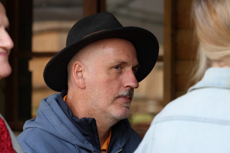 Mann mit schwarzem Hut im Gespräch mit einer Person in heller Jacke