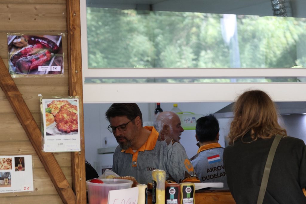 Helfer mit orangefarbenen Halstüchern bereiten in der Vereinsküche Essen zu