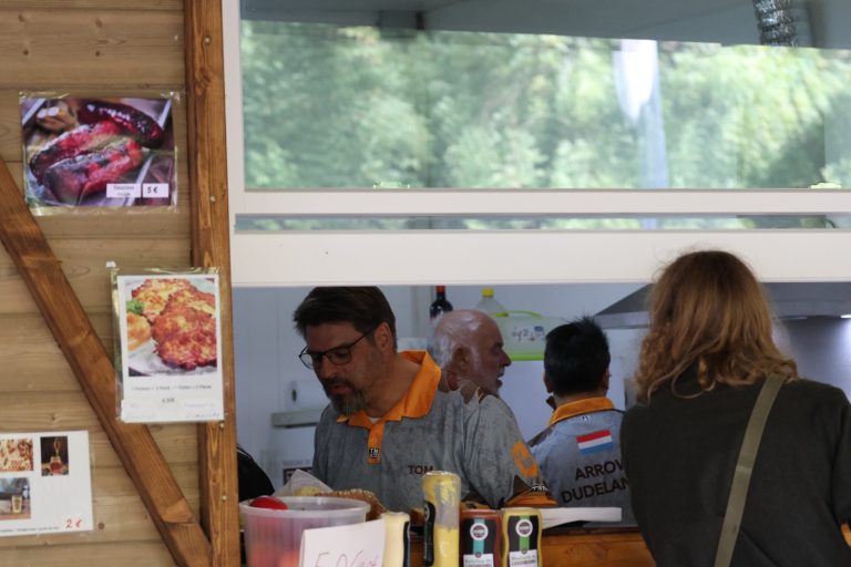 Helfer mit orangefarbenen Halstüchern bereiten in der Vereinsküche Essen zu