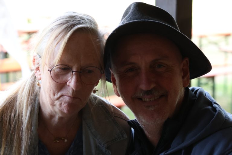Frau mit Brille und Mann mit schwarzem Hut posieren gemeinsam für ein Foto