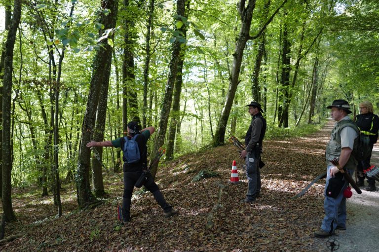 Bogenschütze spannt den Bogen am Hang, Gruppenmitglieder schauen zu