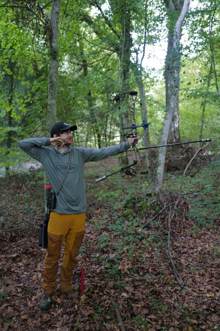 Bogenschütze mit Kappe und gelber Hose spannt einen Compoundbogen im Wald