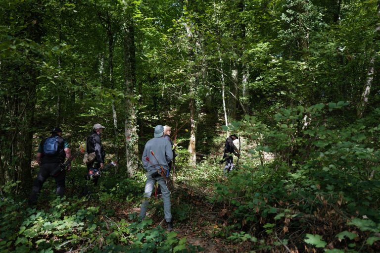 Vier Bogenschützen gehen durch dichten Laubwald zur nächsten Station