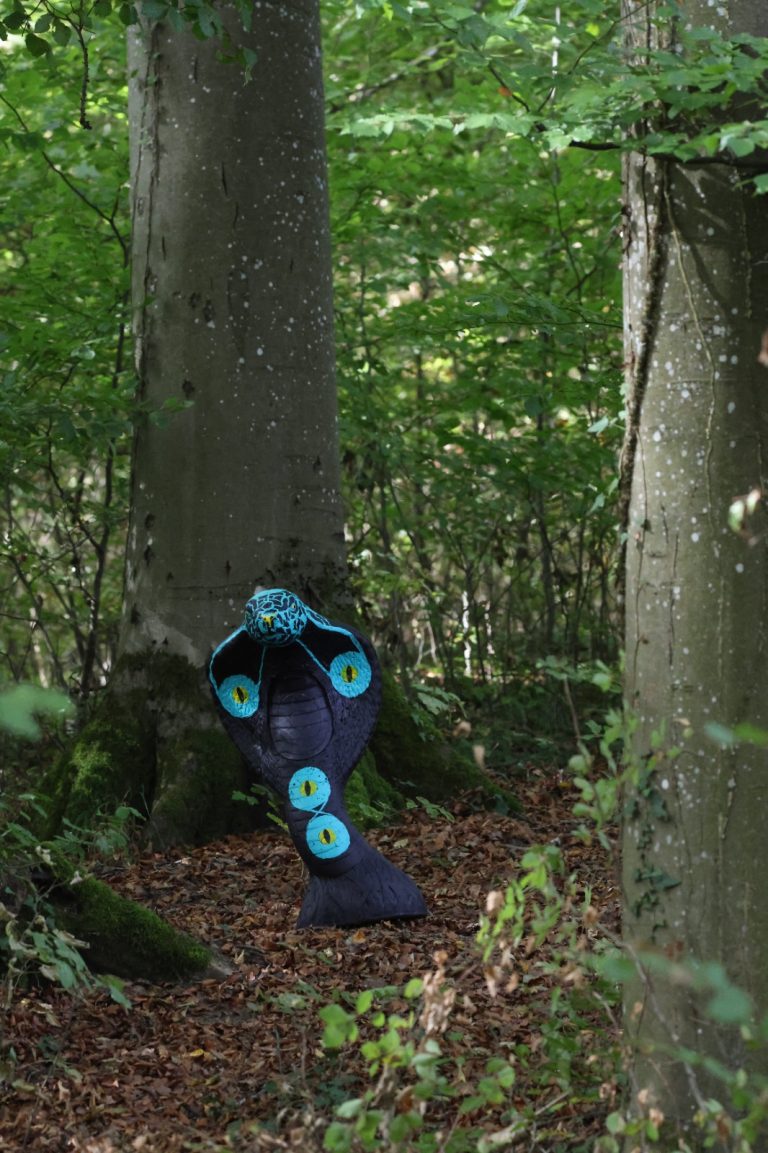Blaues 3D-Kobraziel mit aufgestelltem Nackenschild zwischen Buchenstämmen