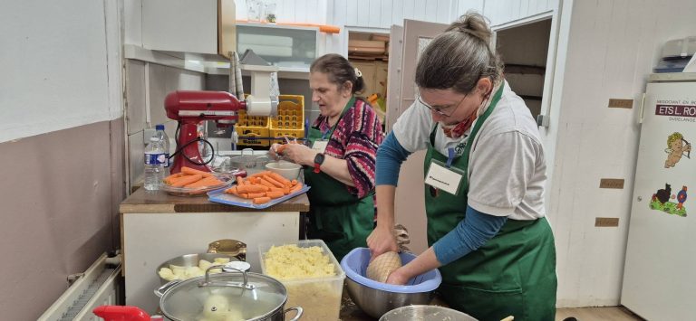 Zwei Helferinnen mit grünen Schürzen bereiten in der Vereinsküche das Essen zu