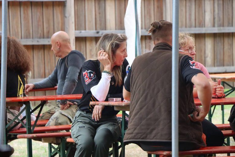 Teilnehmer sitzen unter dem Zelt an Bierbänken vor dem Holzzaun