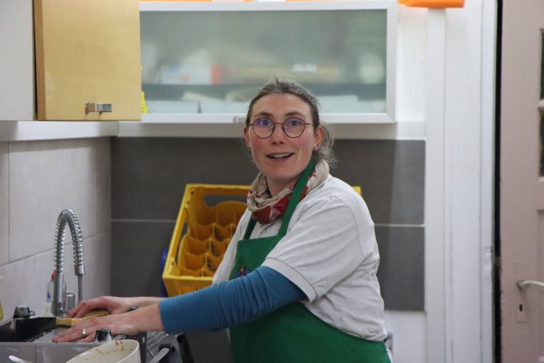 Frau mit Brille und grüner Schürze lacht an der Spüle der Vereinsküche
