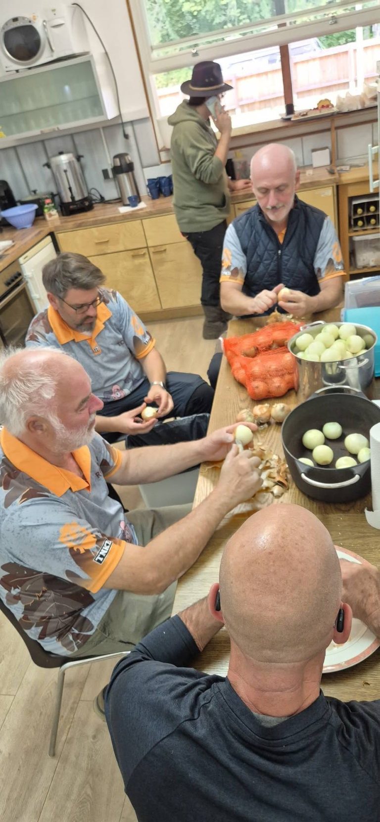 Vereinsmitglieder sitzen am Tisch mit Tomaten, Zwiebeln und Töpfen und bereiten das Essen vor