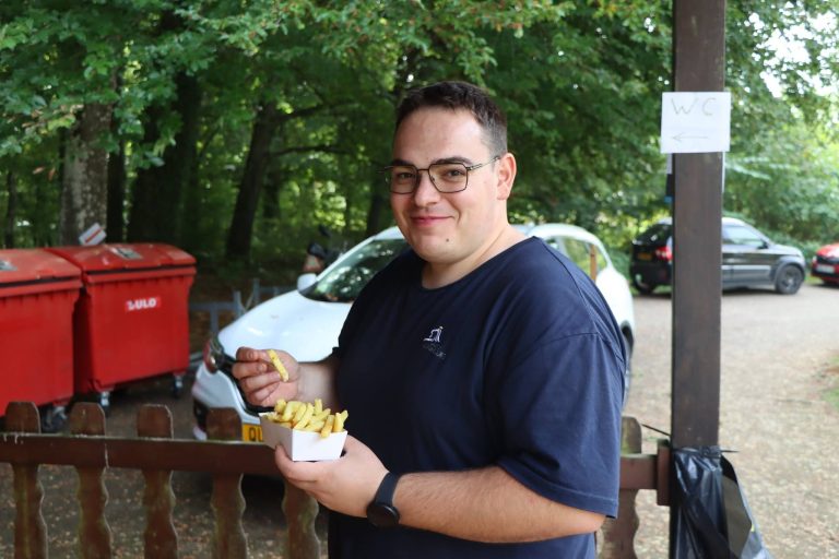 Junger Mann mit Brille hält lächelnd eine Schale Pommes