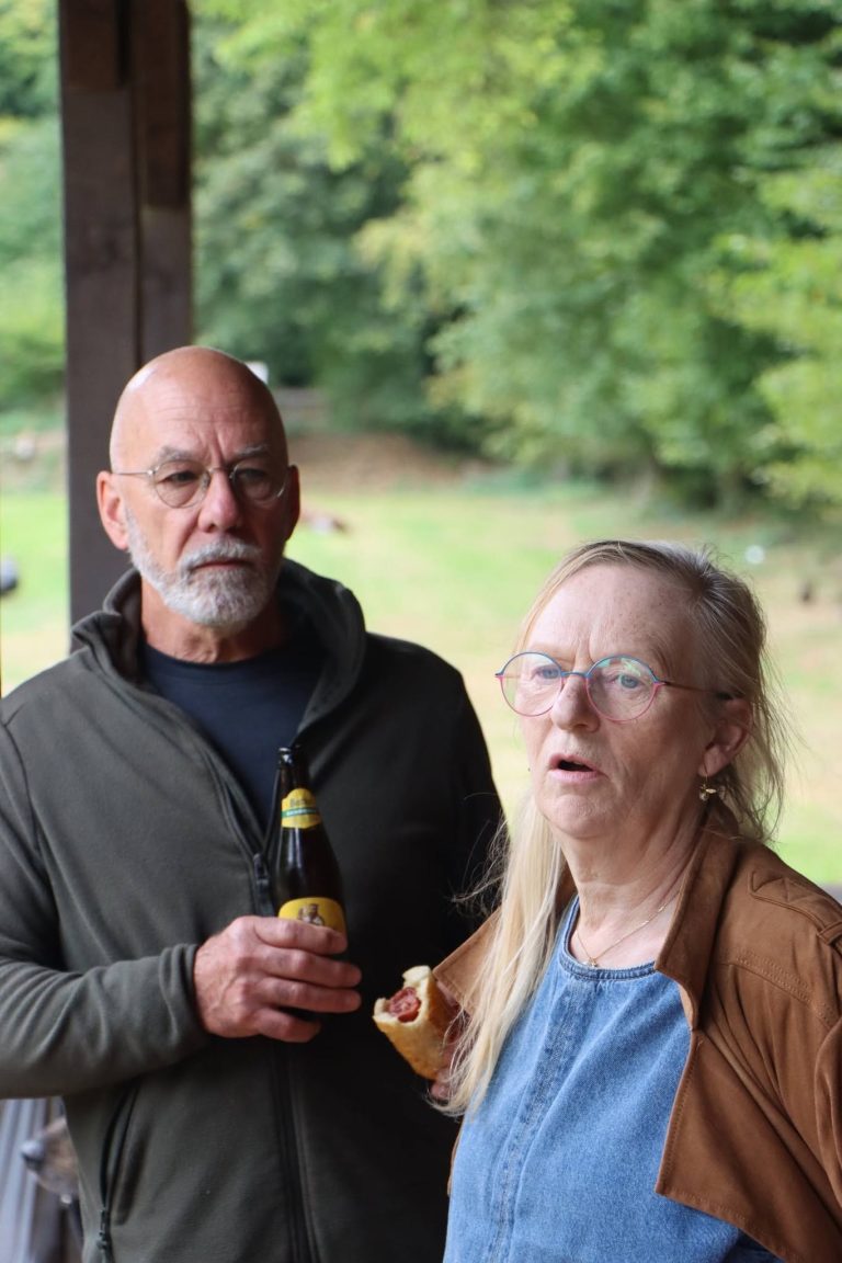 Mann mit Glatze und Frau mit langen grauen Haaren stehen mit einem Getränk beisammen