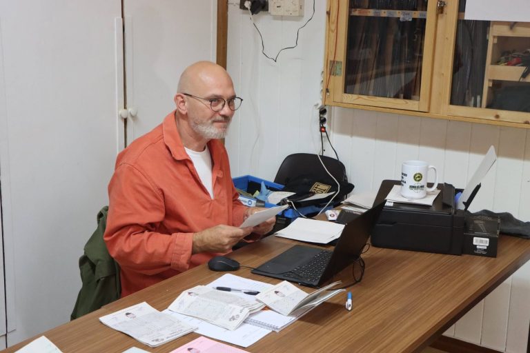 Mann in orangefarbenem Hemd sitzt mit Laptop und Drucker am Tisch im Vereinshaus