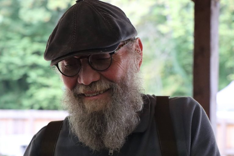 Lächelnder Mann mit grauem Vollbart, Brille und Schiebermütze