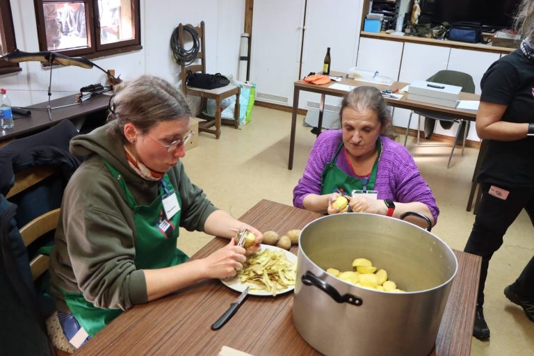 Zwei Helferinnen schälen am Tisch Kartoffeln in einen großen Topf