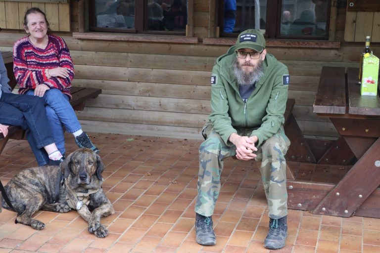 Teilnehmer sitzen auf der Terrasse des Vereinshauses, davor liegt ein gestromter Hund