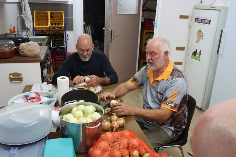 Zwei Mitglieder schneiden am Küchentisch Zwiebeln und Tomaten